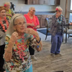 Residents at Stoney Point Meadows participate in a fun hula-themed activity, wearing colorful leis and flowers while engaging in movement and socializing.