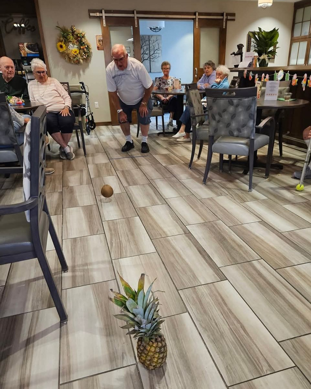 A resident enthusiastically participates in a fun indoor bowling game using a coconut and a pineapple.