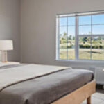 Bright, modern senior living bedroom at Stoney Point Meadows with large windows, neutral décor and comfortable furnishings.