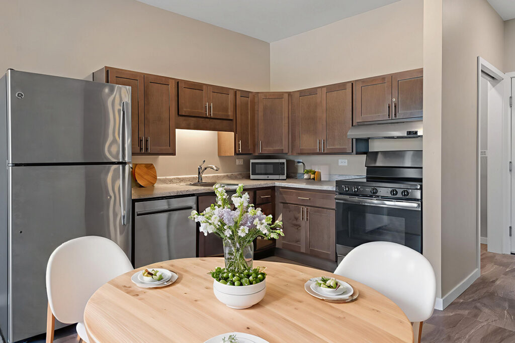 Apartment kitchen with wood cabinets, stainless steel appliances, and a round dining table with place settings in a modern living space at Stoney Point Meadows