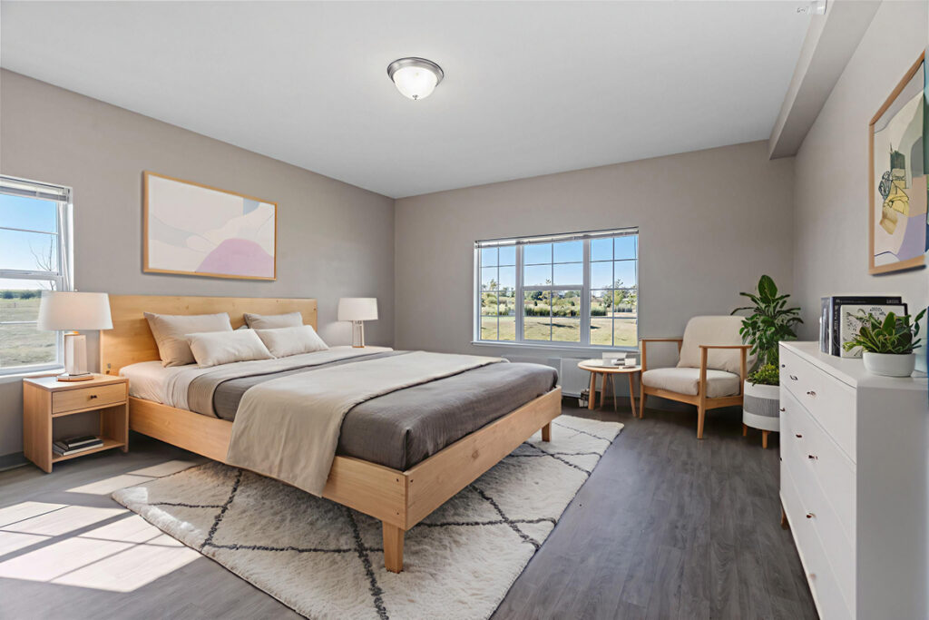 Apartment bedroom with a large bed, nightstands, dresser, seating chair, and window letting in natural light with an outdoor view at Stoney Point Meadows
