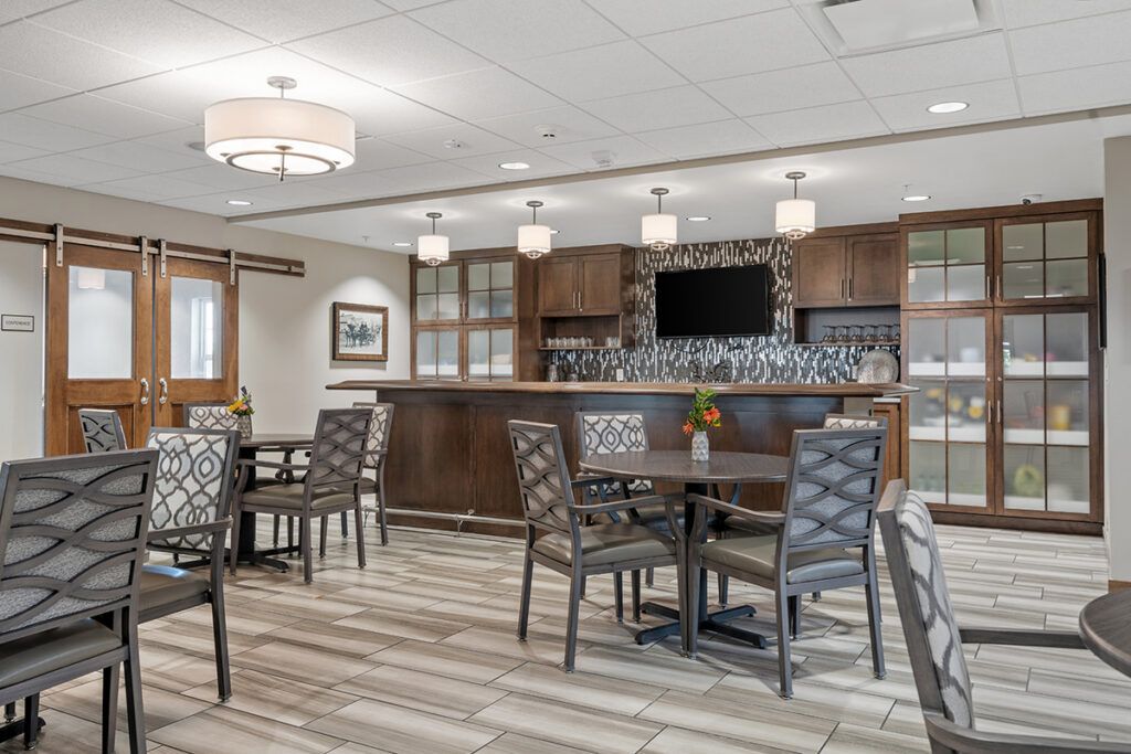 Cafe-style bistro area with round tables, chairs, bar counter, cabinetry, and wall-mounted television in a social gathering space at Stoney Point Meadows