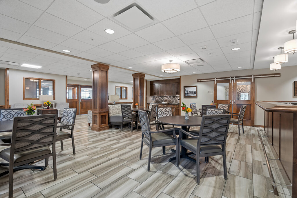 Open bistro and lounge area with round tables, chairs, wood columns, bar counter, and connecting seating spaces at Stoney Point Meadows