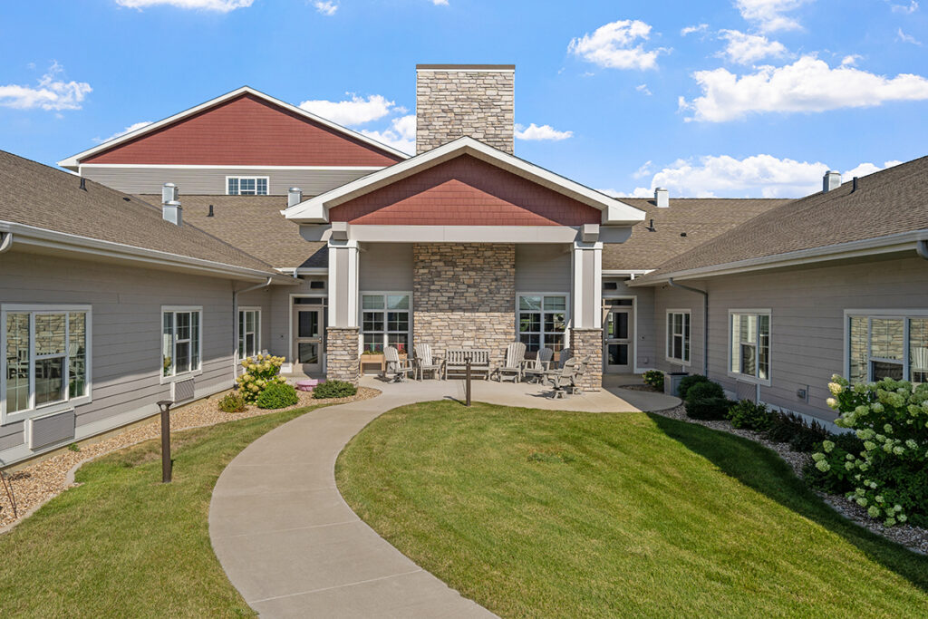 Courtyard garden with a curved walking path, green lawn, outdoor seating, and covered patio entrance at Stoney Point Meadows