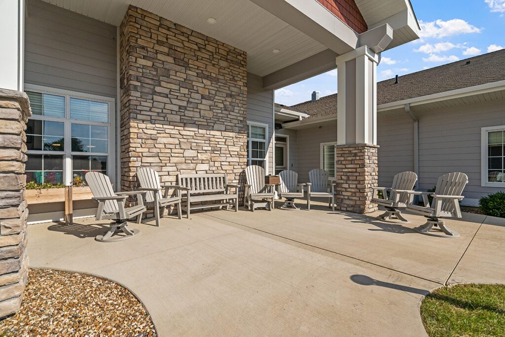 Covered outdoor patio with multiple chairs, a bench, and stone columns near the building entrance at Stoney Point Meadows
