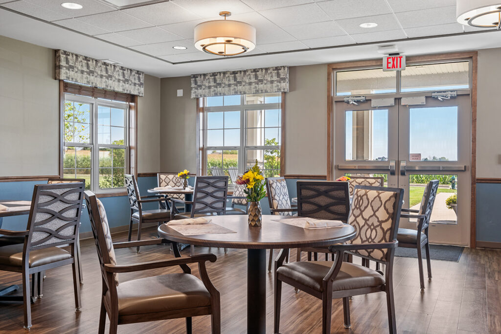 Dining room with round tables, chairs, flower centerpieces, large windows, and double doors leading outside at Stoney Point Meadows