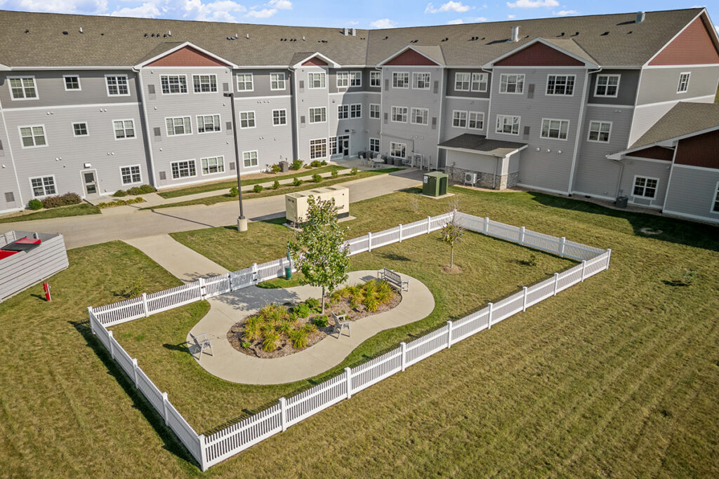 Aerial view of a fenced courtyard garden with a walking path, benches, landscaped greenery, and surrounding residential building at Stoney Point Meadows