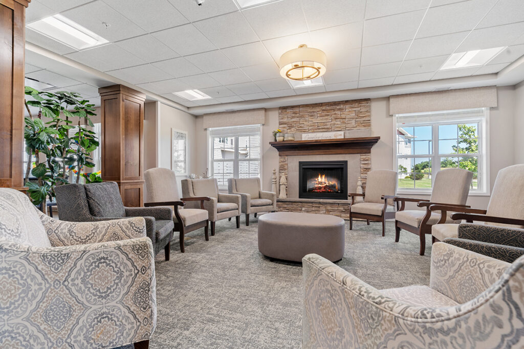 Circular seating arrangement with upholstered chairs around a fireplace, surrounded by windows and wood columns in a lounge space at Stoney Point Meadows
