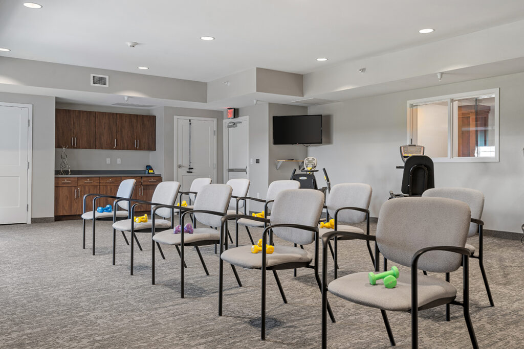 Fitness and activity room with rows of chairs, hand weights on seats, exercise equipment, television, and cabinetry at Stoney Point Meadows