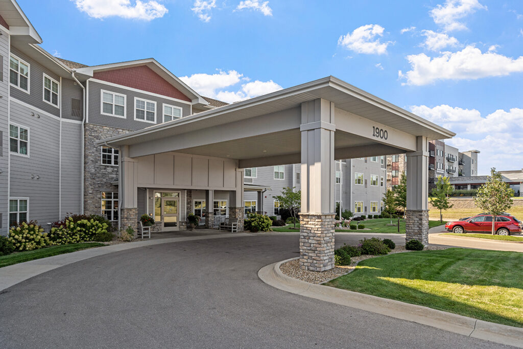 Front entrance exterior with covered drop-off canopy, columns, landscaped grounds, and building facade at Stoney Point Meadows
