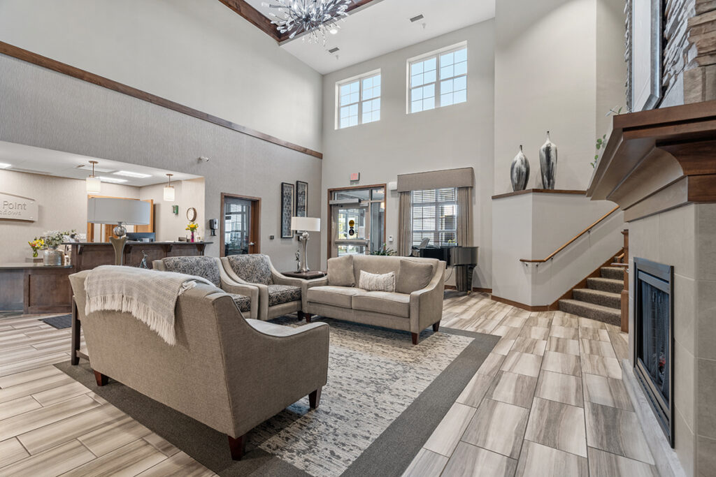 Lobby seating area with sofas, armchairs, area rug, fireplace, staircase, and large windows in a bright, open space at Stoney Point Meadows