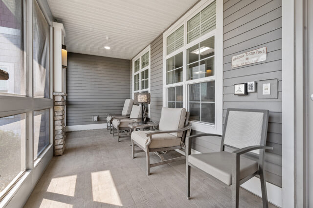 Screened-in porch with cushioned chairs, side table, stone column, and large windows along the exterior of the building at Stoney Point Meadows