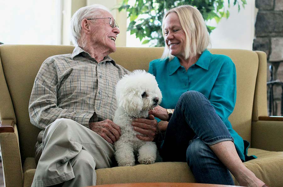 Two older adults seated together on a couch in a living room setting, representing social interaction and comfortable living like at Stoney Point Meadows