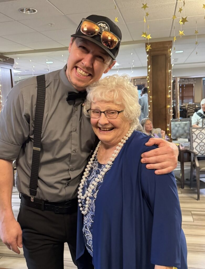 Staff member and resident pose together in formal attire at a prom-themed celebration.