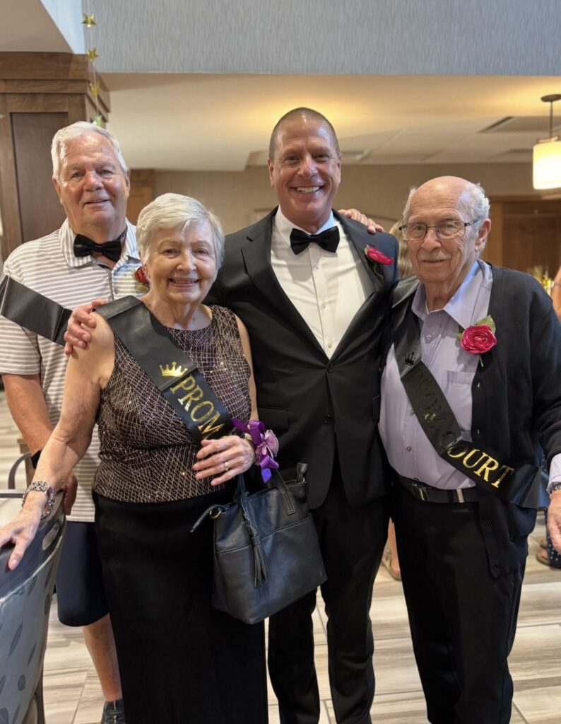 Prom court members and a guest in formal attire pose together at a prom-themed celebration.